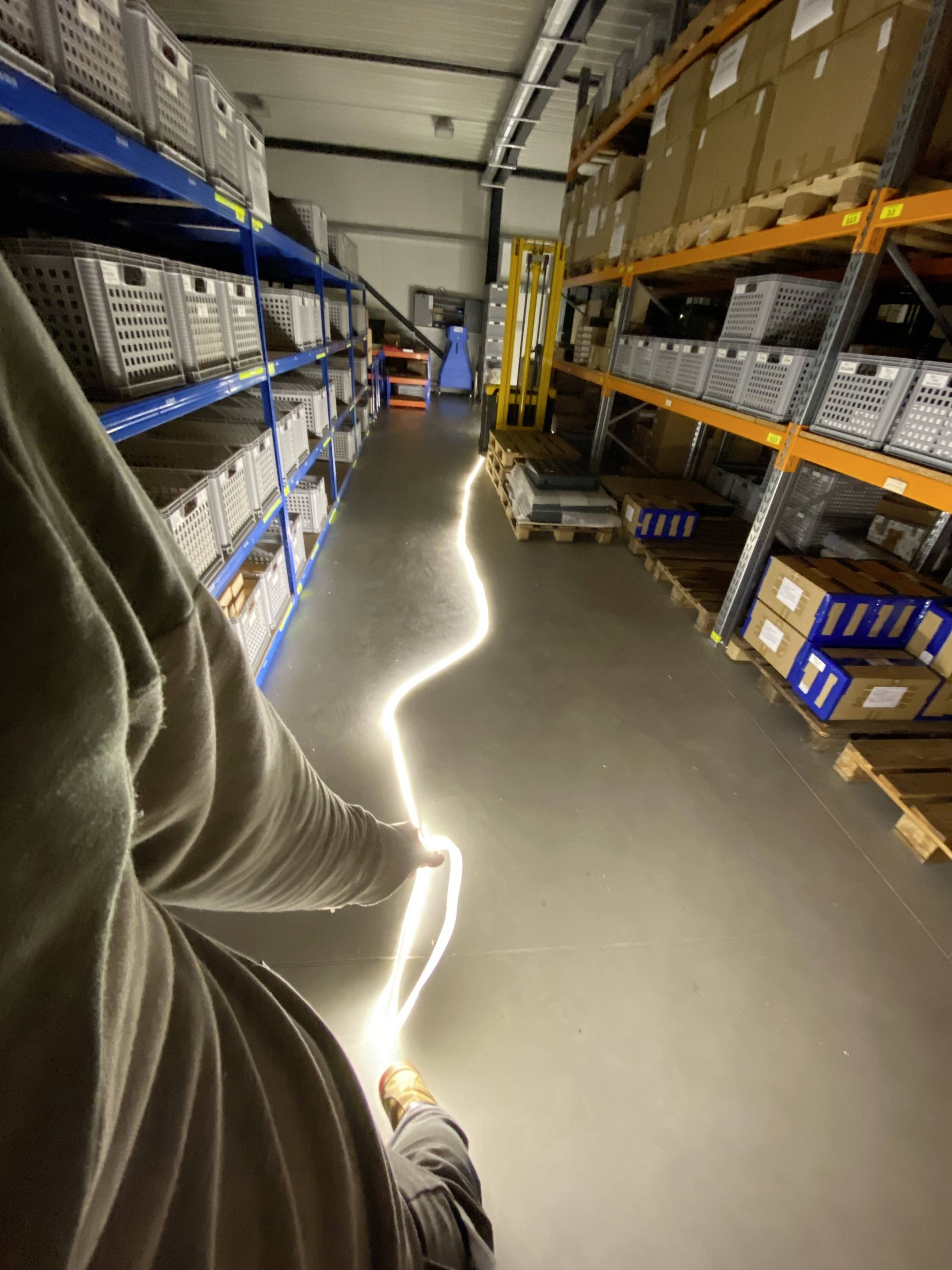 A person is pulling a glowing rope through a storage room with shelves full of boxes and cartons.