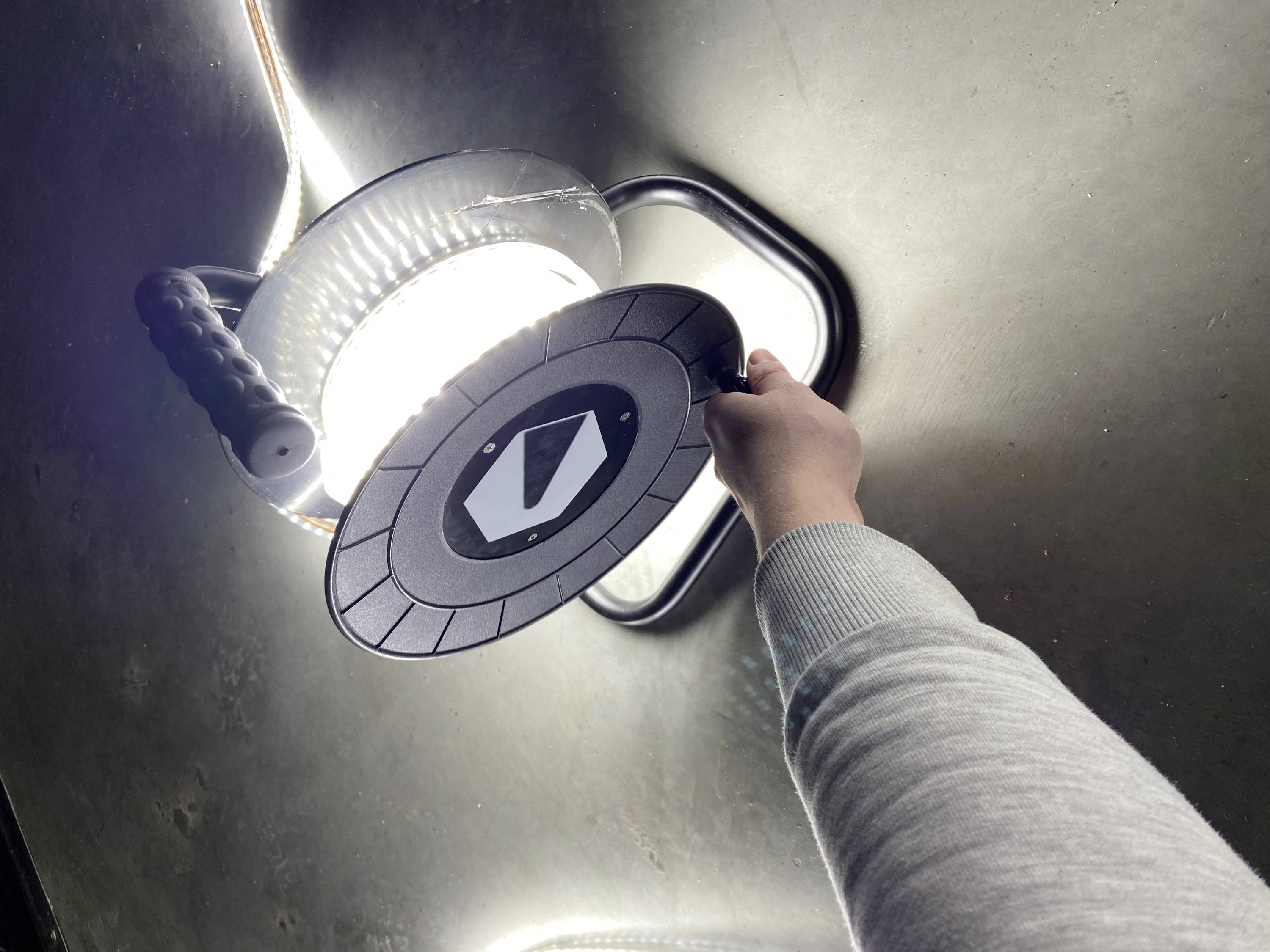 A hand holds the end of a coiled cable reel. The reel is lying on a grey floor and is brightly illuminated.