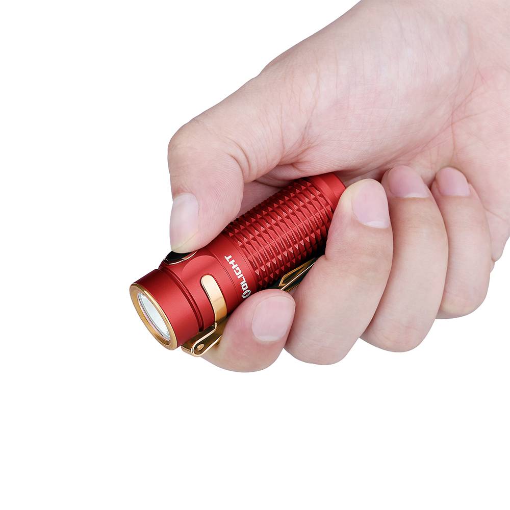 Red torch is held by a hand. It is compact, cylindrical and has a bright light at the front.