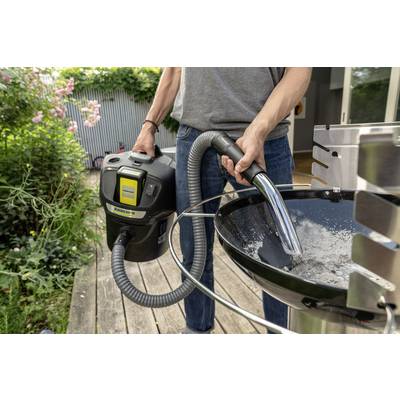 A person is vacuuming ash from a barbecue using a handheld ash vacuum. Plants can be seen in the background.