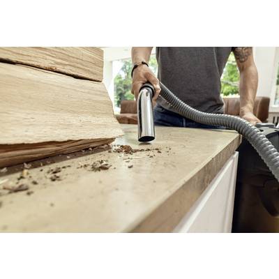 A person is vacuuming wood dust and dirt from a workbench. Large wooden boards are visible in the background.