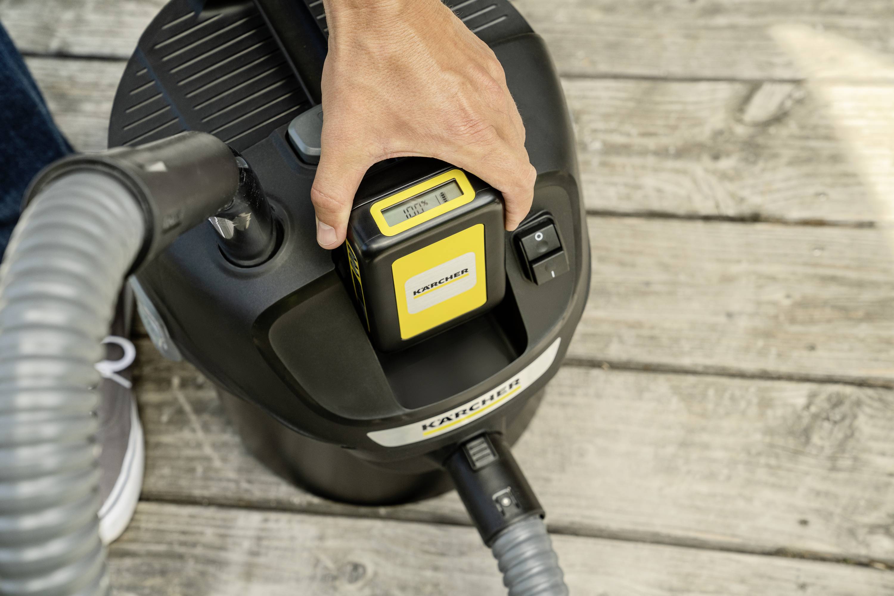 A person is inserting a battery into a cordless vacuum cleaner standing on a wooden floor.