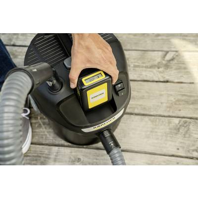 A person is inserting a battery into a cordless vacuum cleaner standing on a wooden floor.