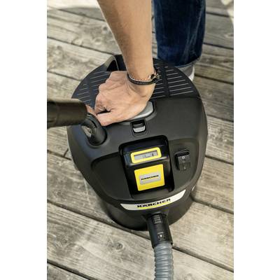 A person is cleaning a wooden terrace with a wet/dry vacuum cleaner. A hand is holding the handle of the device. The device is standing on the terrace.