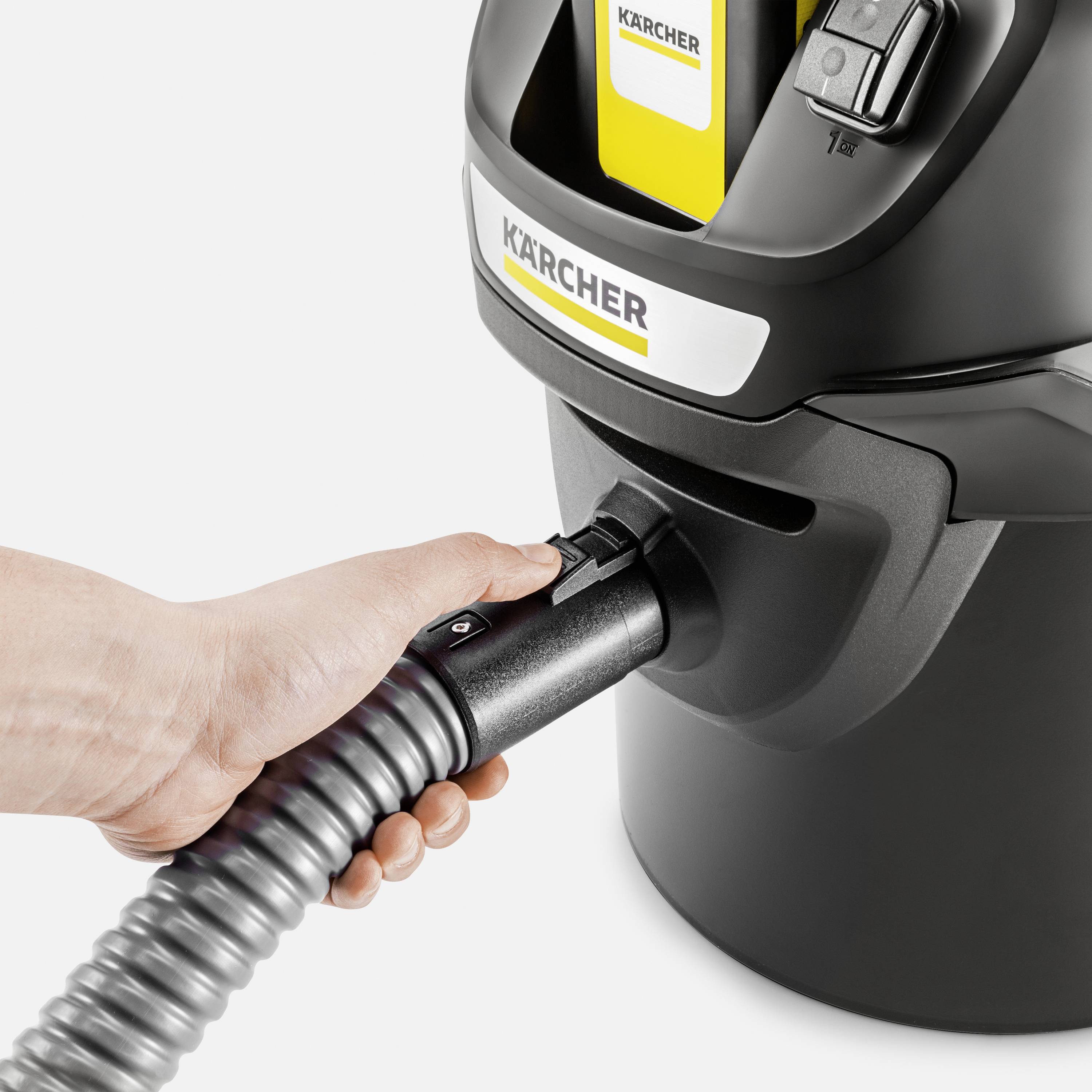 A hand is holding a hose connected to a Kärcher vacuum cleaner. The device appears robust and industrial.