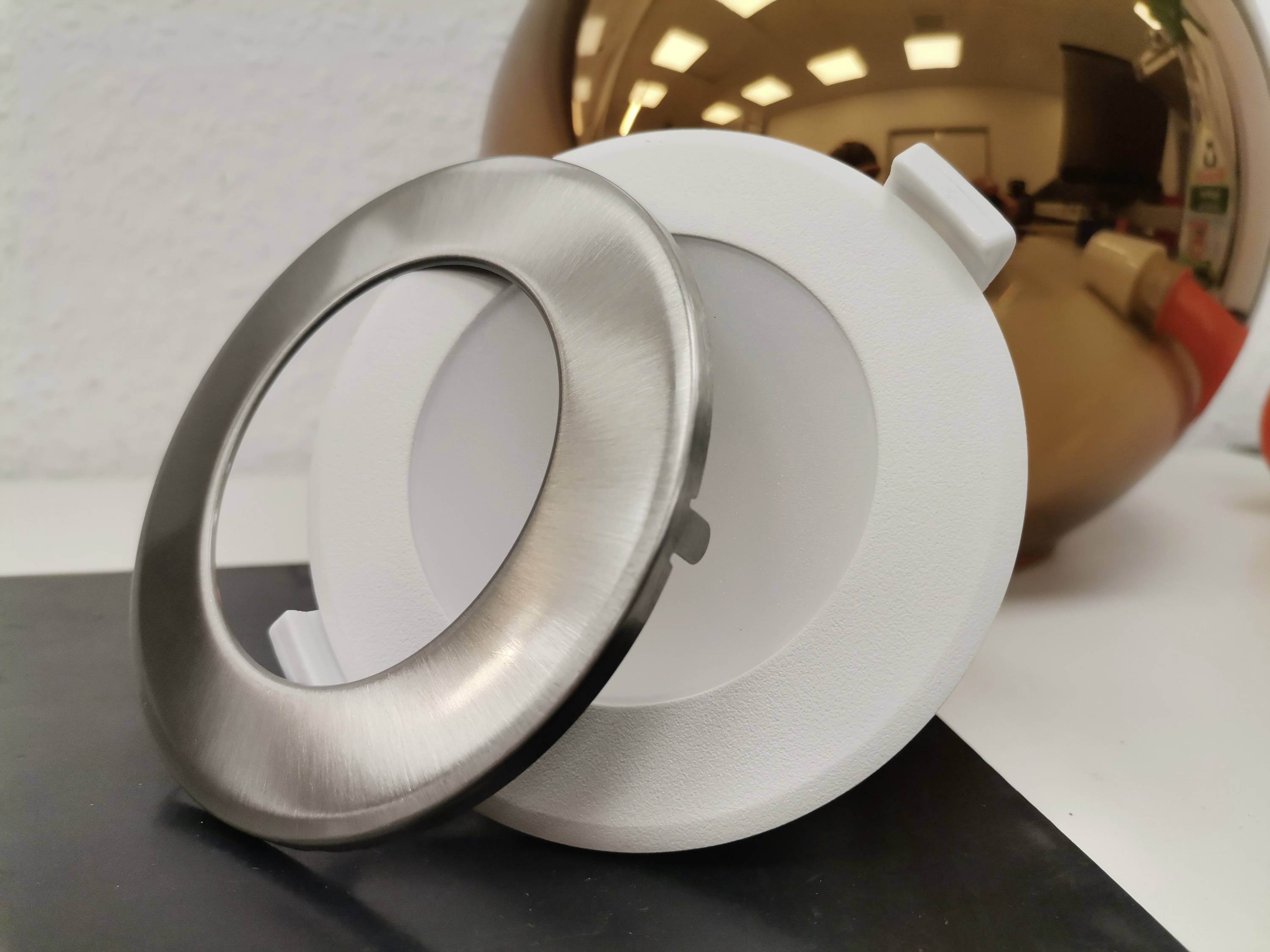 Two round covers, one made of silver metal and one made of white plastic, are lying side by side on a table.