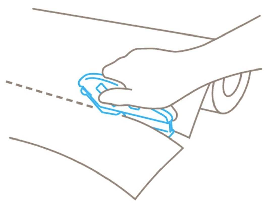 A hand is cutting along a dotted line with a craft knife on a sheet of paper from a roll.