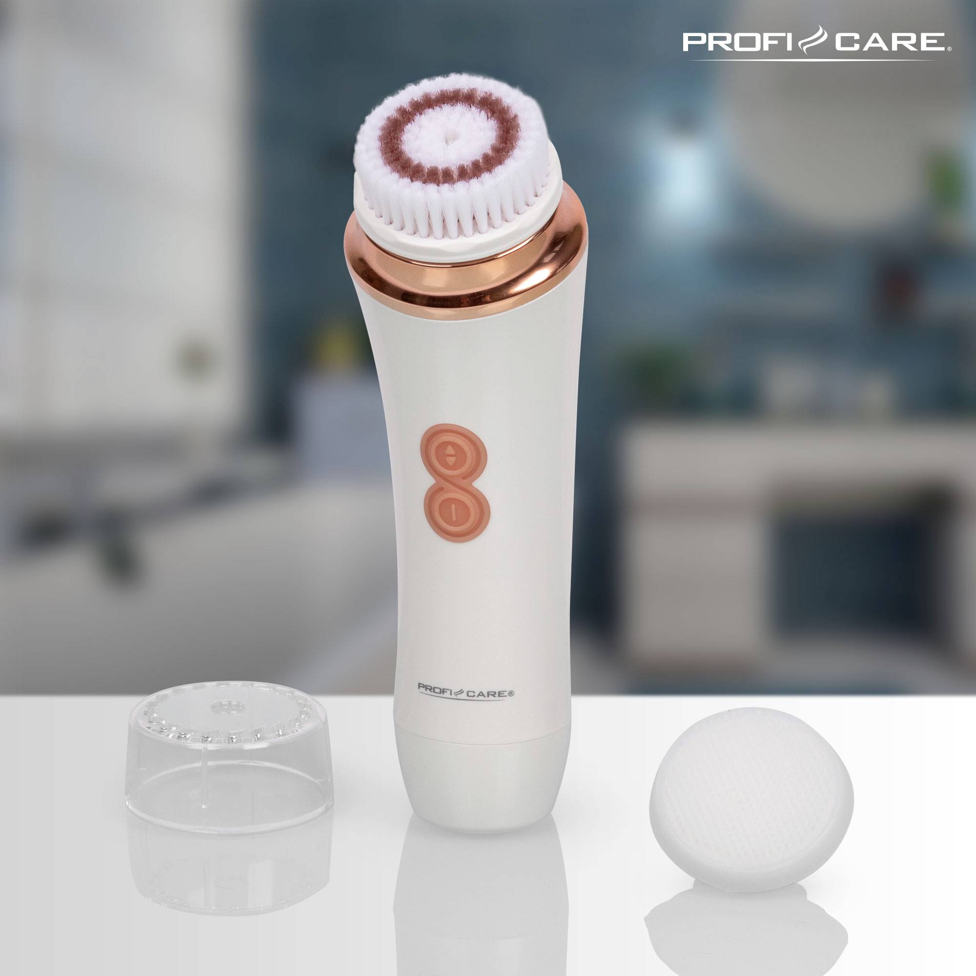 Electric facial cleansing brush with rose gold details and interchangeable brush heads against a blurred bathroom background.