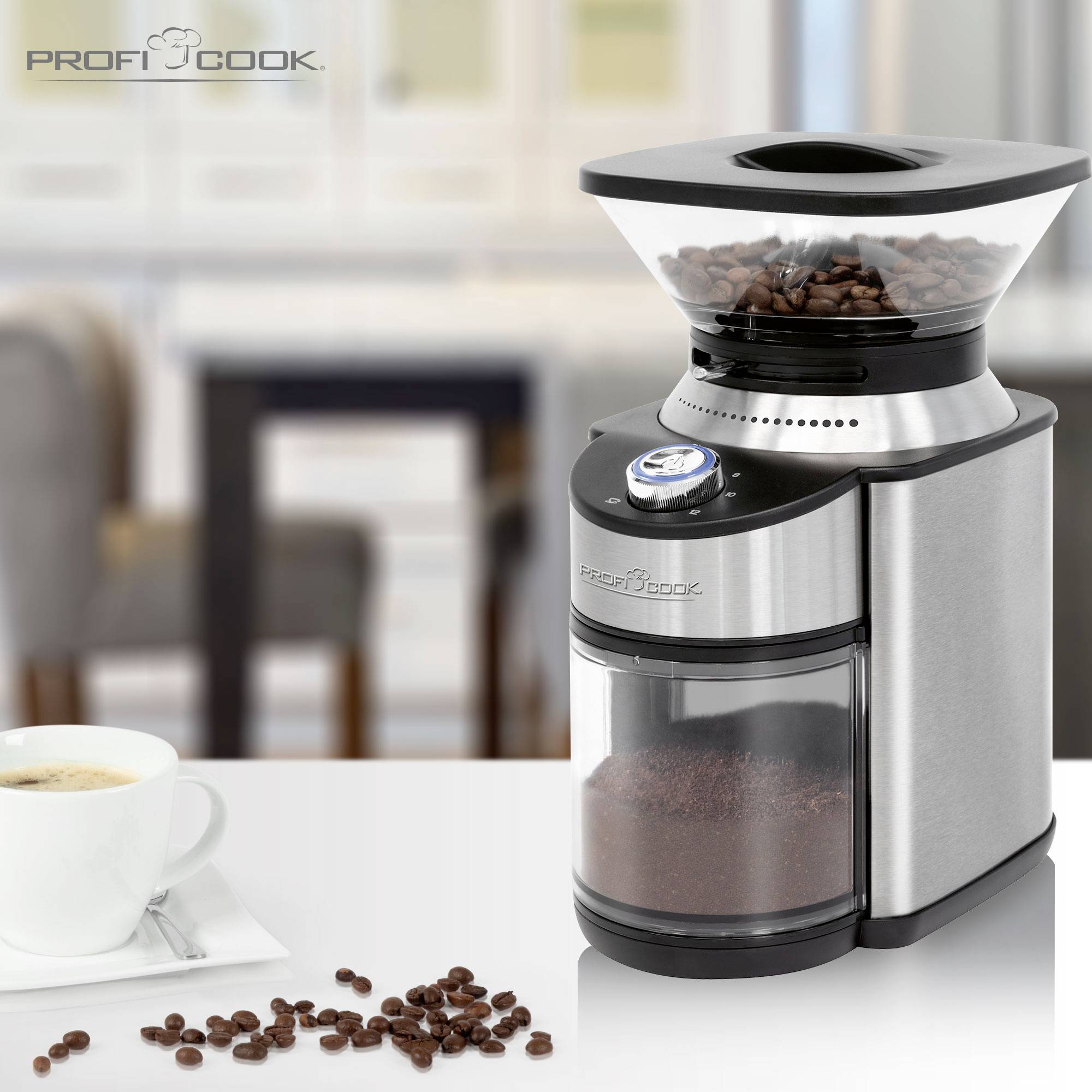 A stainless steel coffee grinder on a kitchen worktop, surrounded by ground coffee and coffee beans, with a cup of coffee beside it.