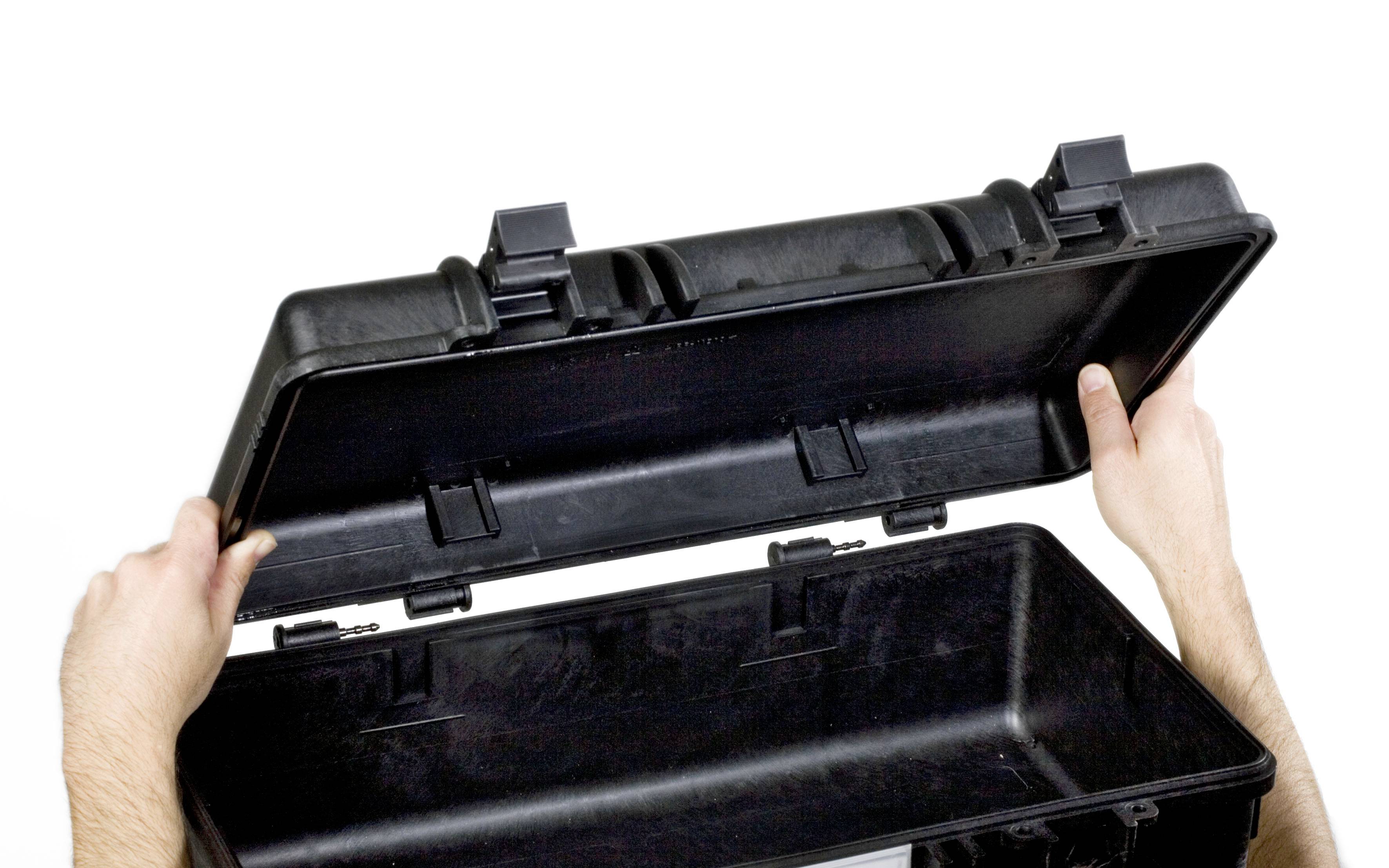 Two hands are opening a black, empty suitcase. The suitcase has robust clasps and is presumably designed for transportation.