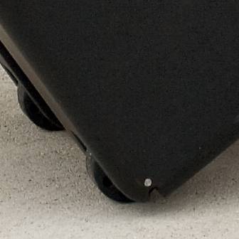 A portion of a black wheeled suitcase on sandy ground.