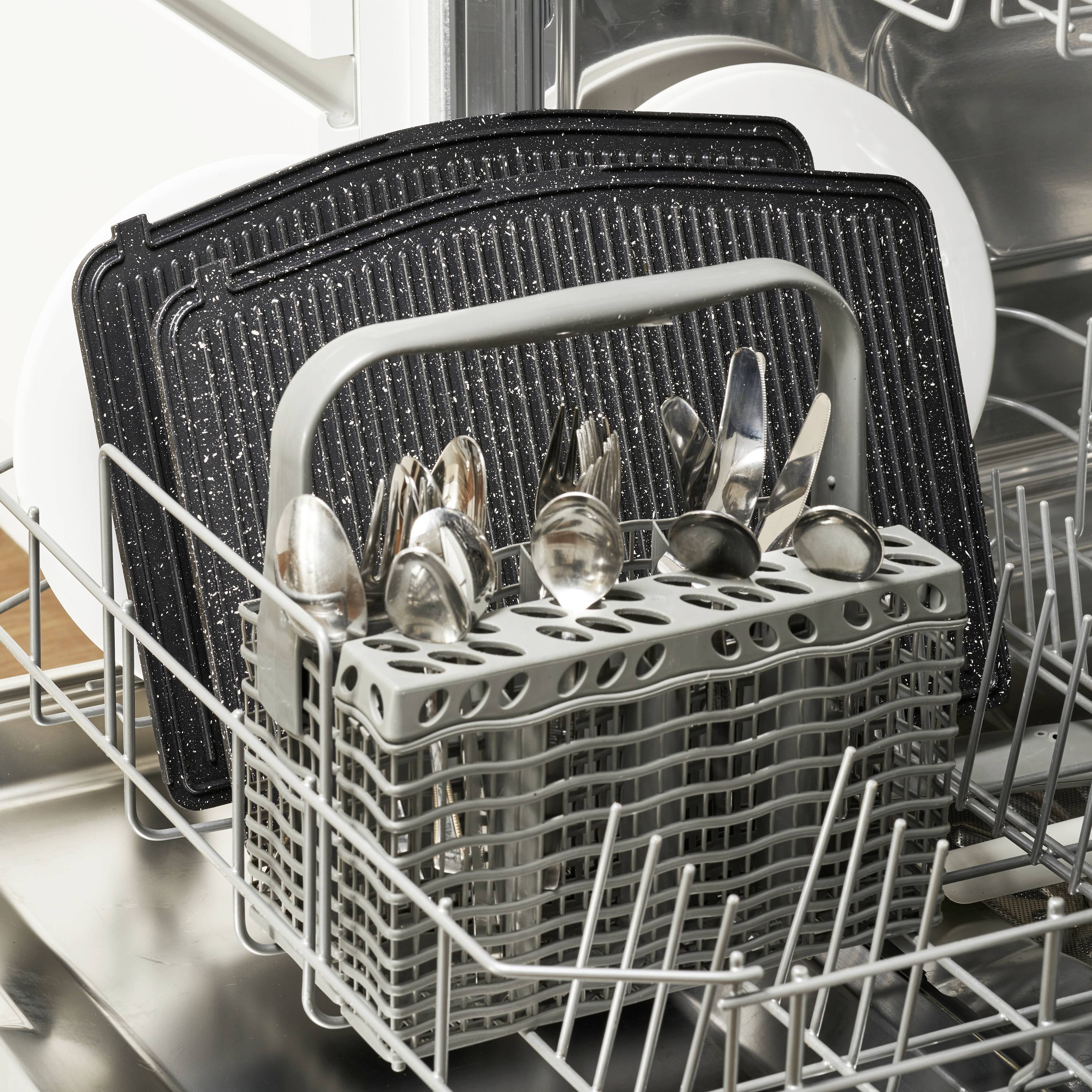 A dishwasher with an open basket shows cutlery in a holder and several black trays in the background.