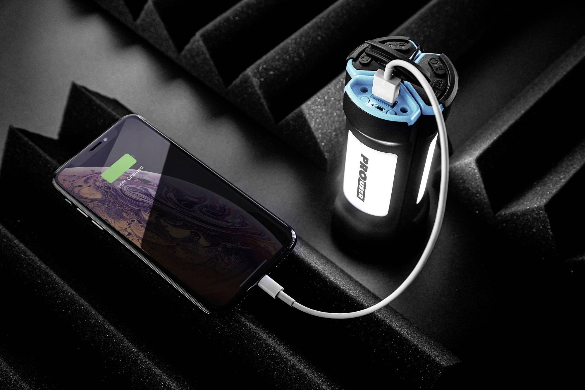 A smartphone is being charged via a cable from a portable power bank resting on a foam-like mat.