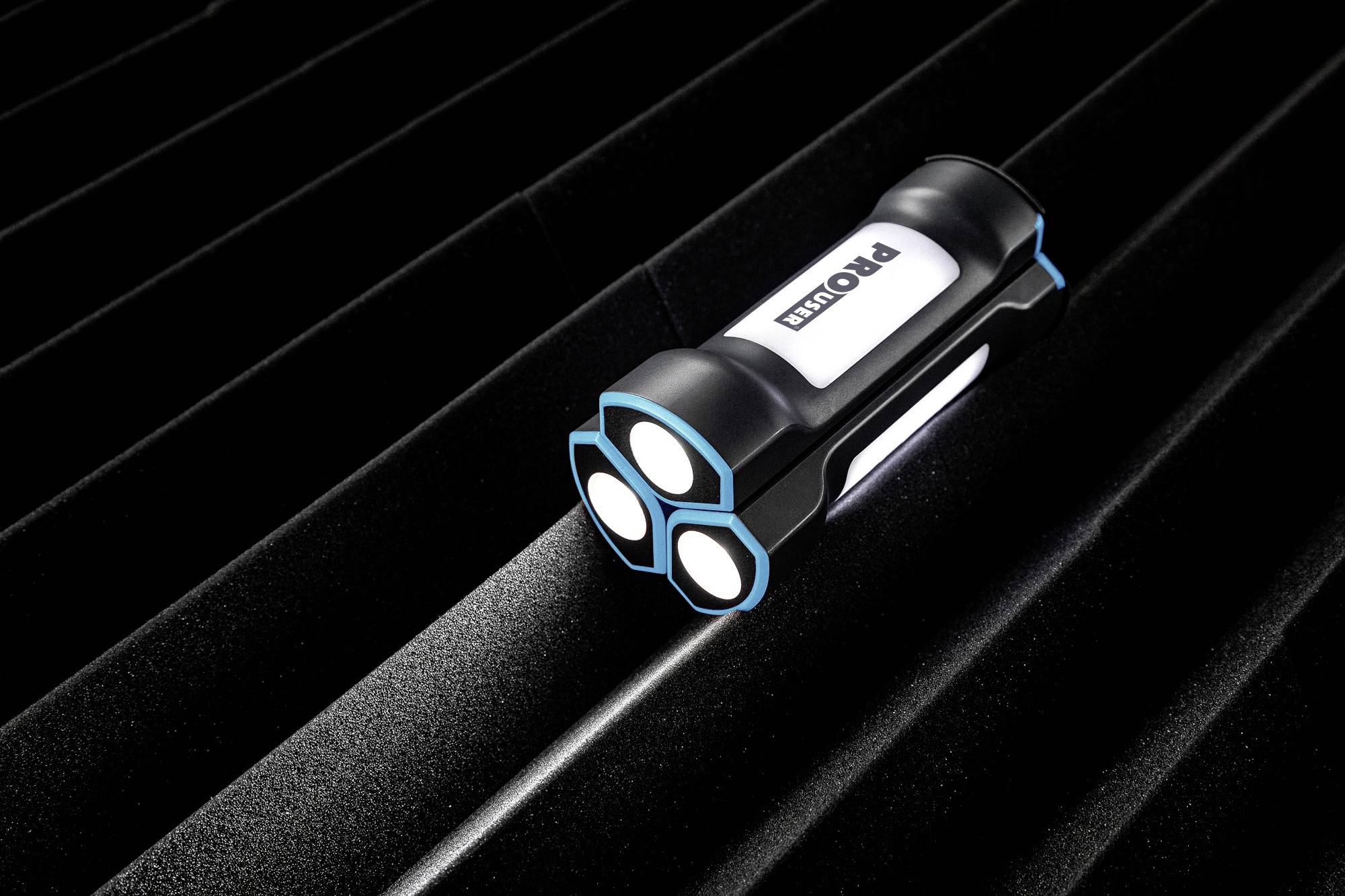 A torch with three bright LED lights lies on a dark, ridged surface.