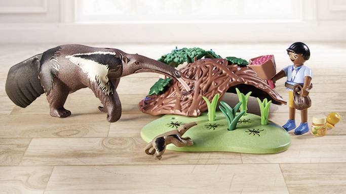 Toy Scene: An anteater and a figurine stand beside a toy hill. In the foreground, a small monkey toy is lying down.