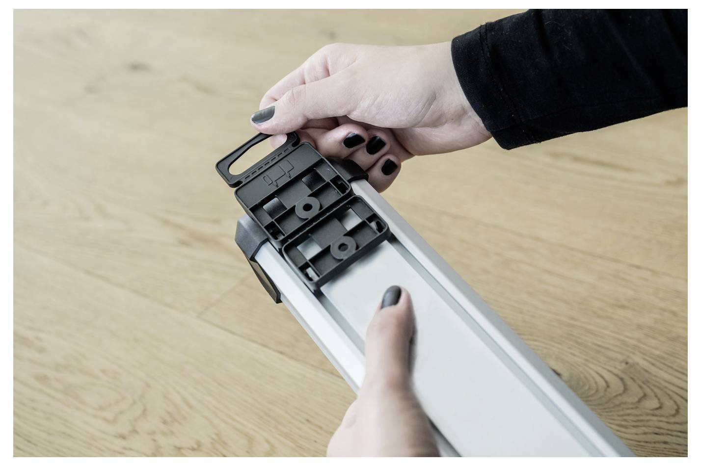 Person adjusting the end cap on a white LED light fixture or strip light on a wooden surface.