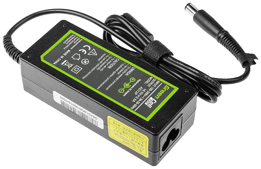 A black laptop power adapter with cable and plug, featuring a green label on the top surface displaying technical specifications and safety symbols.