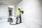 A construction worker in work attire and hard hat is using an electric tool to work on a wall in an unfinished room.