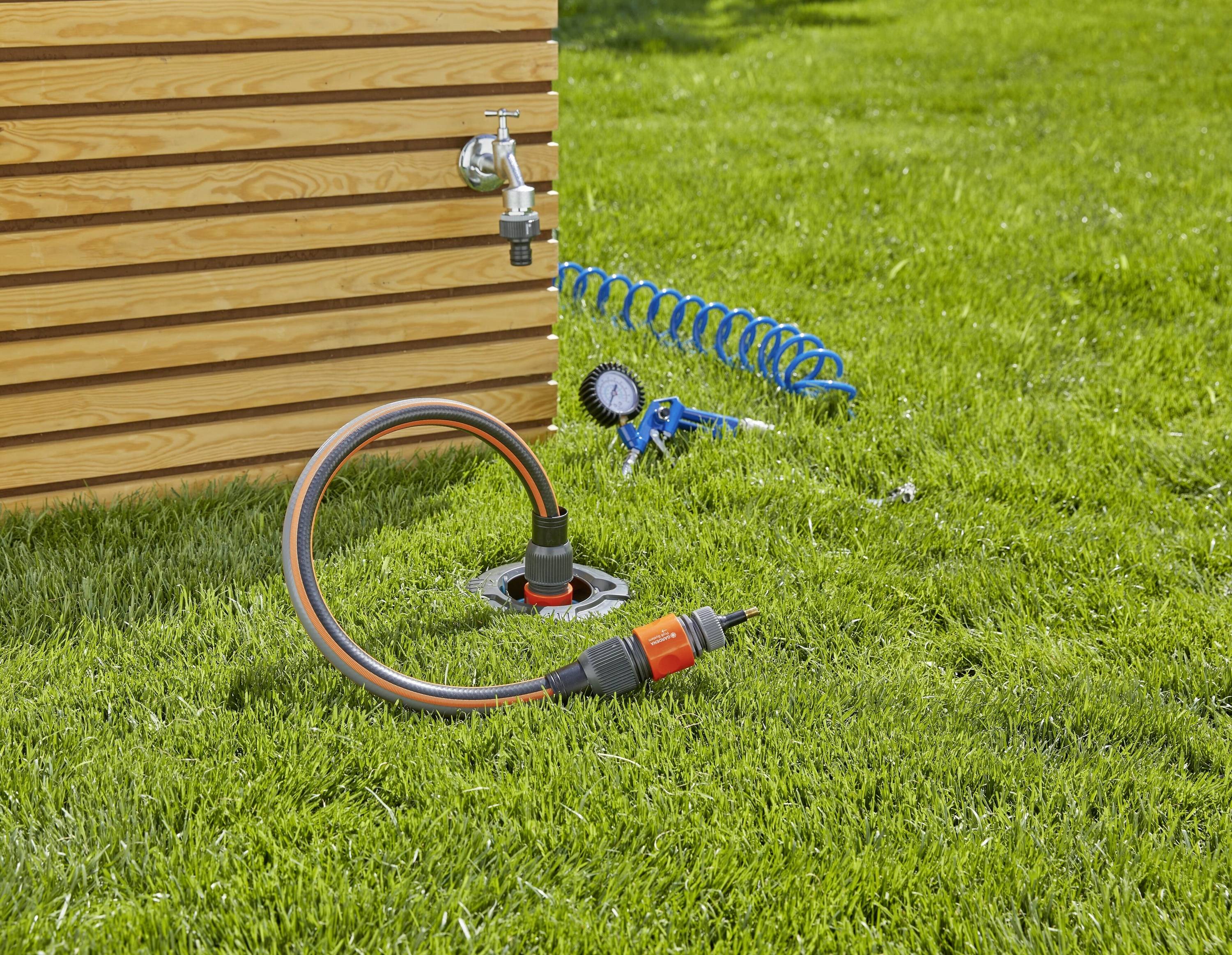 Hosepipe system for garden irrigation with hose, tap, valve and spray nozzle on lawn beside wooden house.