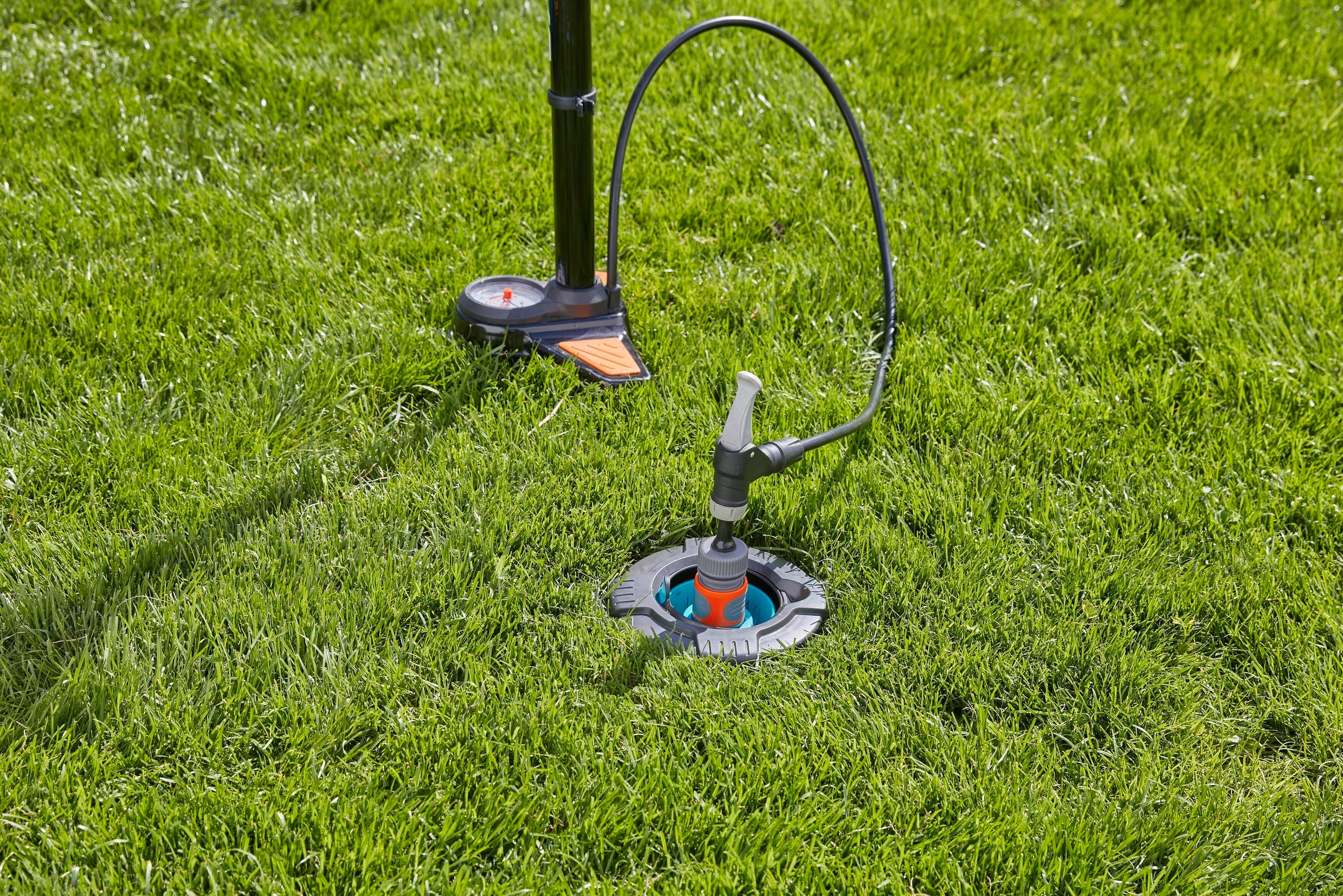 A lawn sprinkler installed on a lawn is controlled by a pressure valve on a stand.