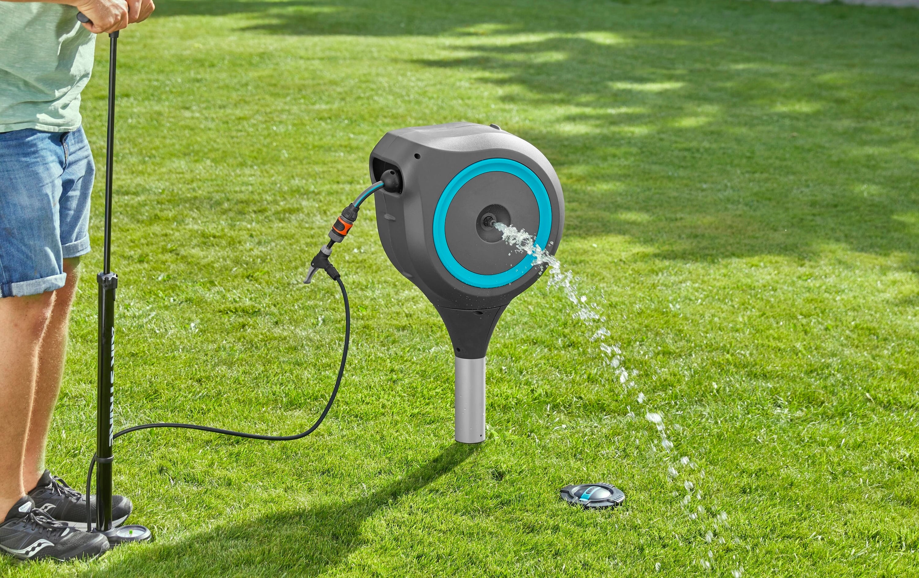 A person is operating a water pump on a lawn. A water hose is connected to a round, blue pump and is spraying water.
