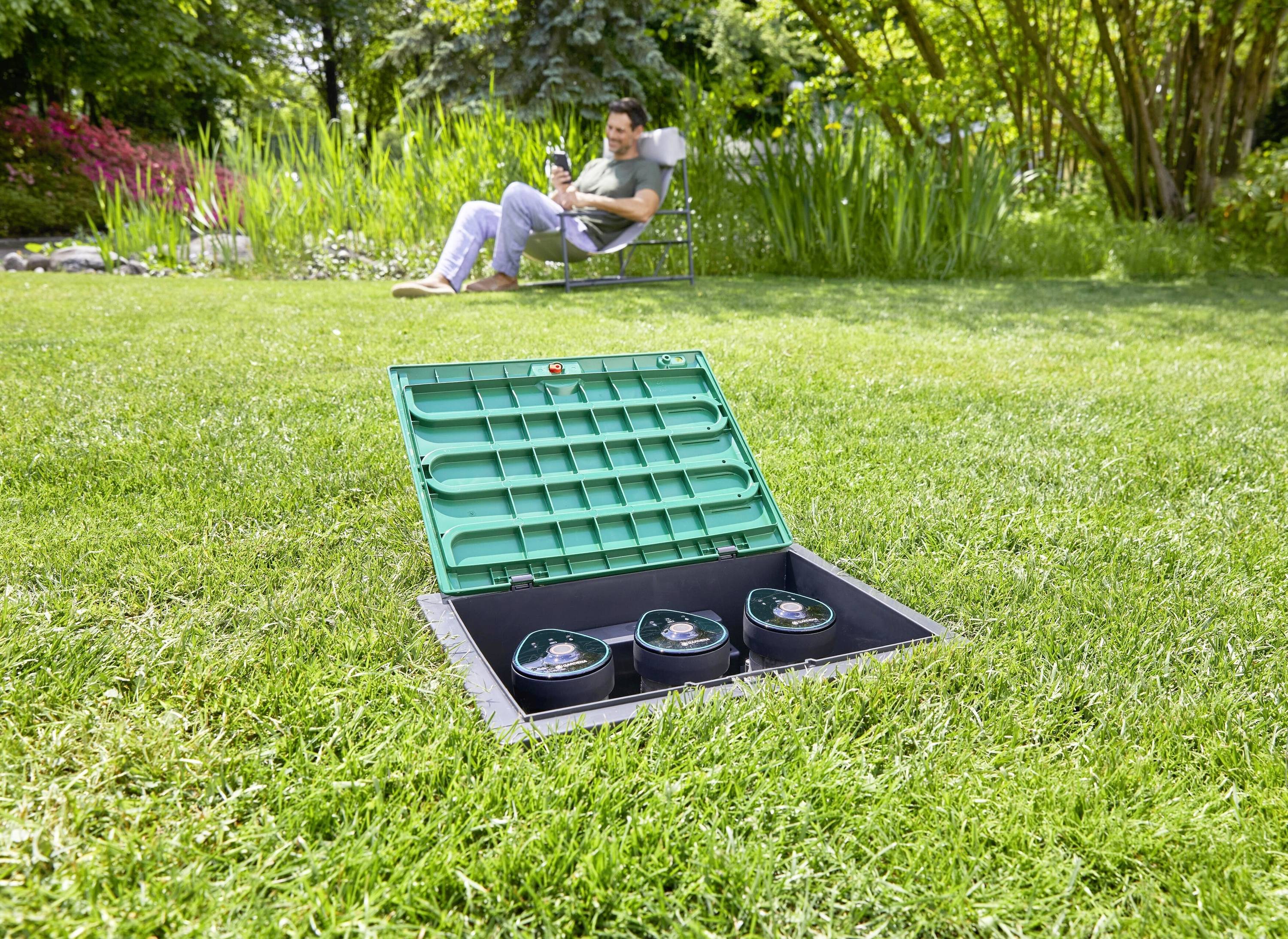 A man is sitting on a chair with a drink, while an open green plastic box is visible in the grass in the foreground.
