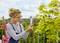 A person wearing glasses and a striped jumper is examining a device on a balcony, surrounded by green plants.