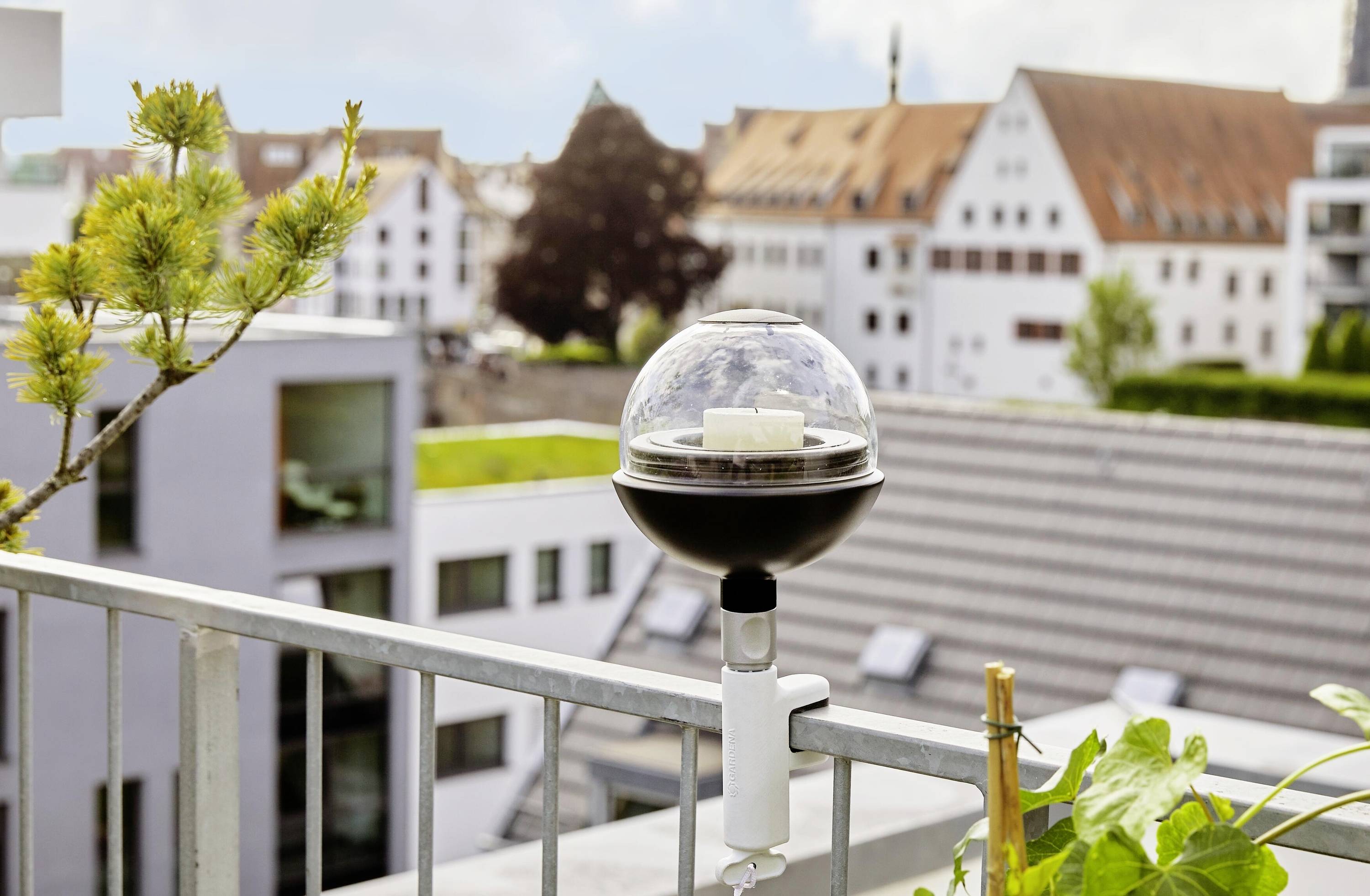 A circular weather monitoring device is mounted on a balcony above an urban area; buildings are visible in the background.