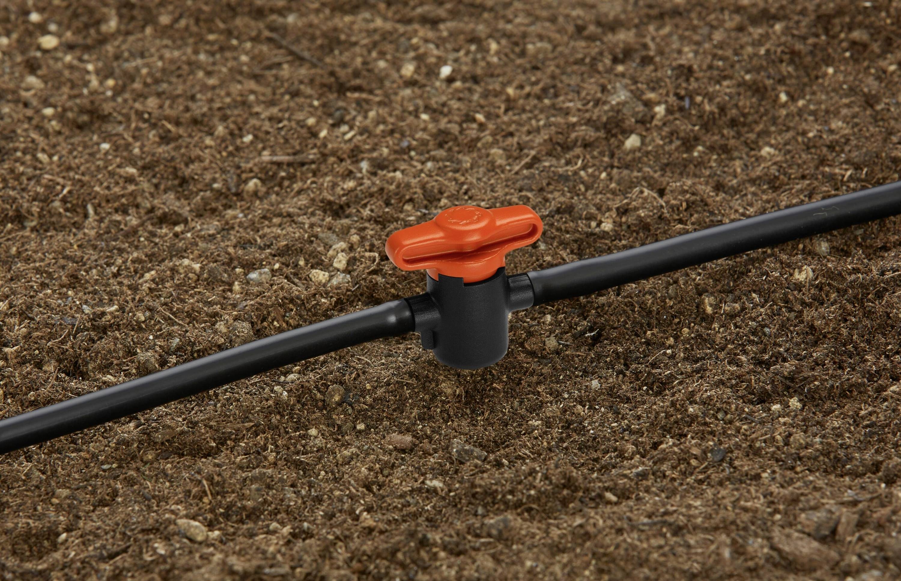 A black irrigation pipe with a red valve on brown earth, part of a drip irrigation system.