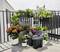 Various flower pots with colourful flowers and plants on a balcony; two black containers are positioned in the foreground.