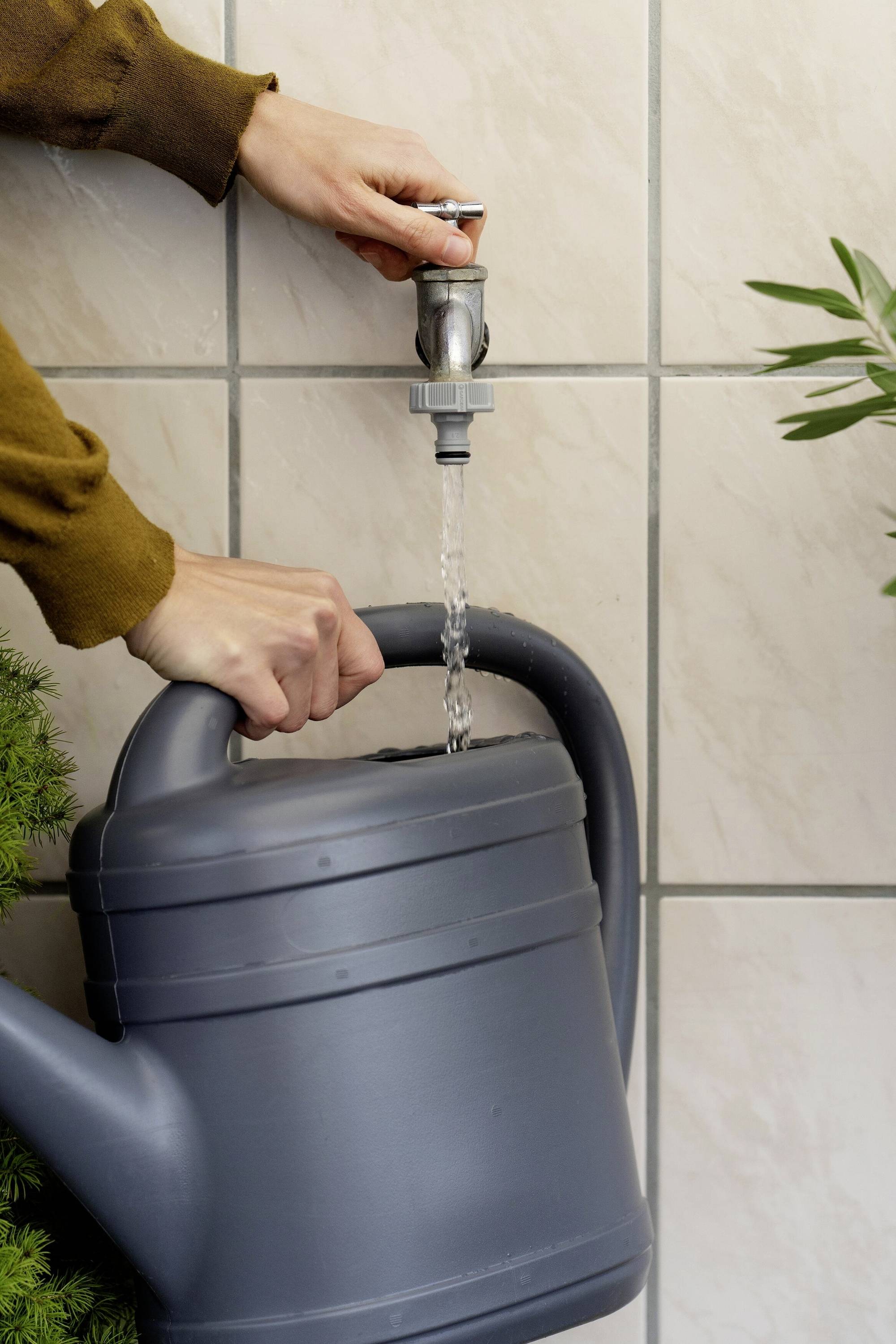 'A person fills a grey watering can with water from a tap.'