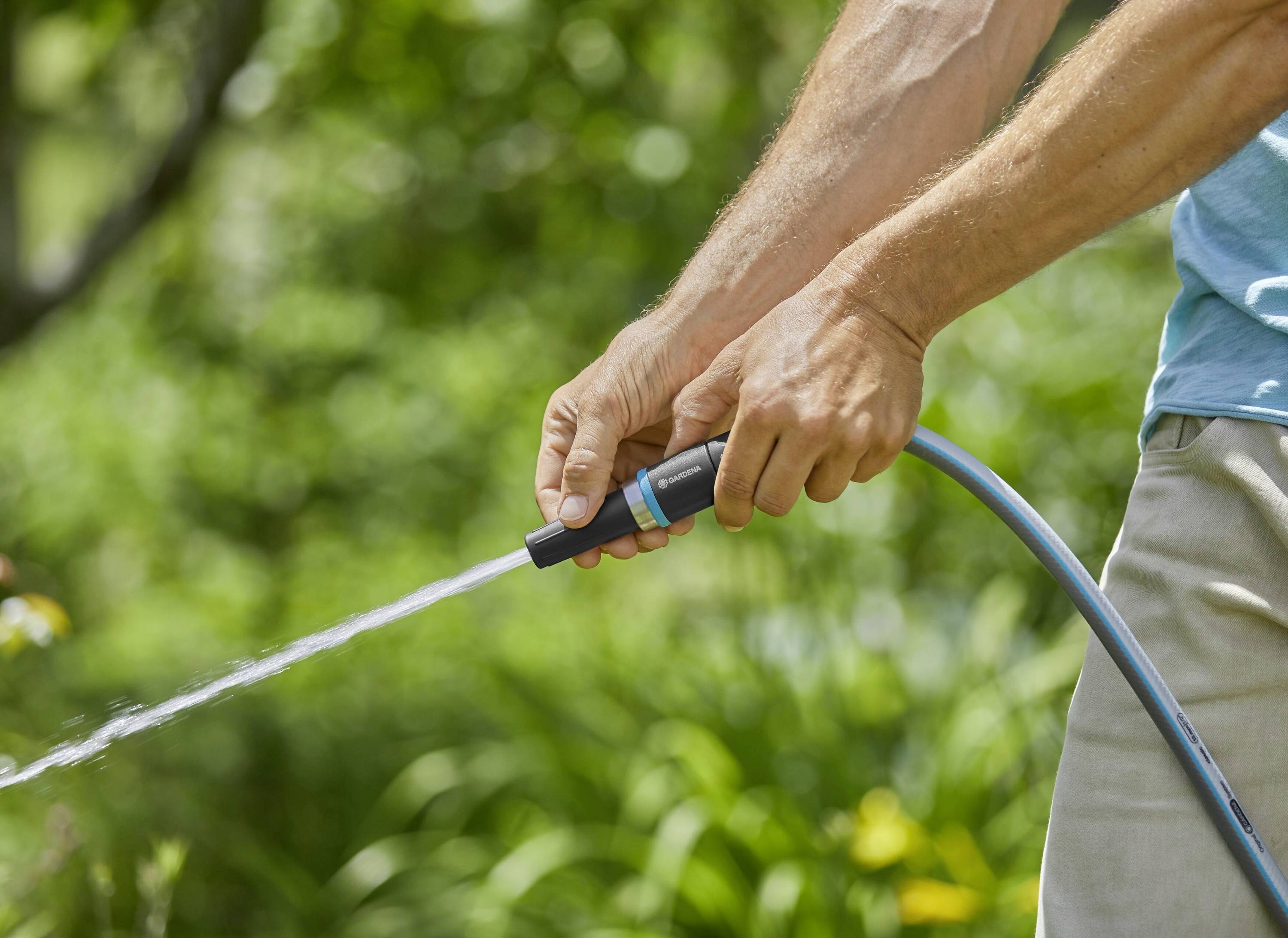 A person is holding a garden hose and spraying water in a green garden.