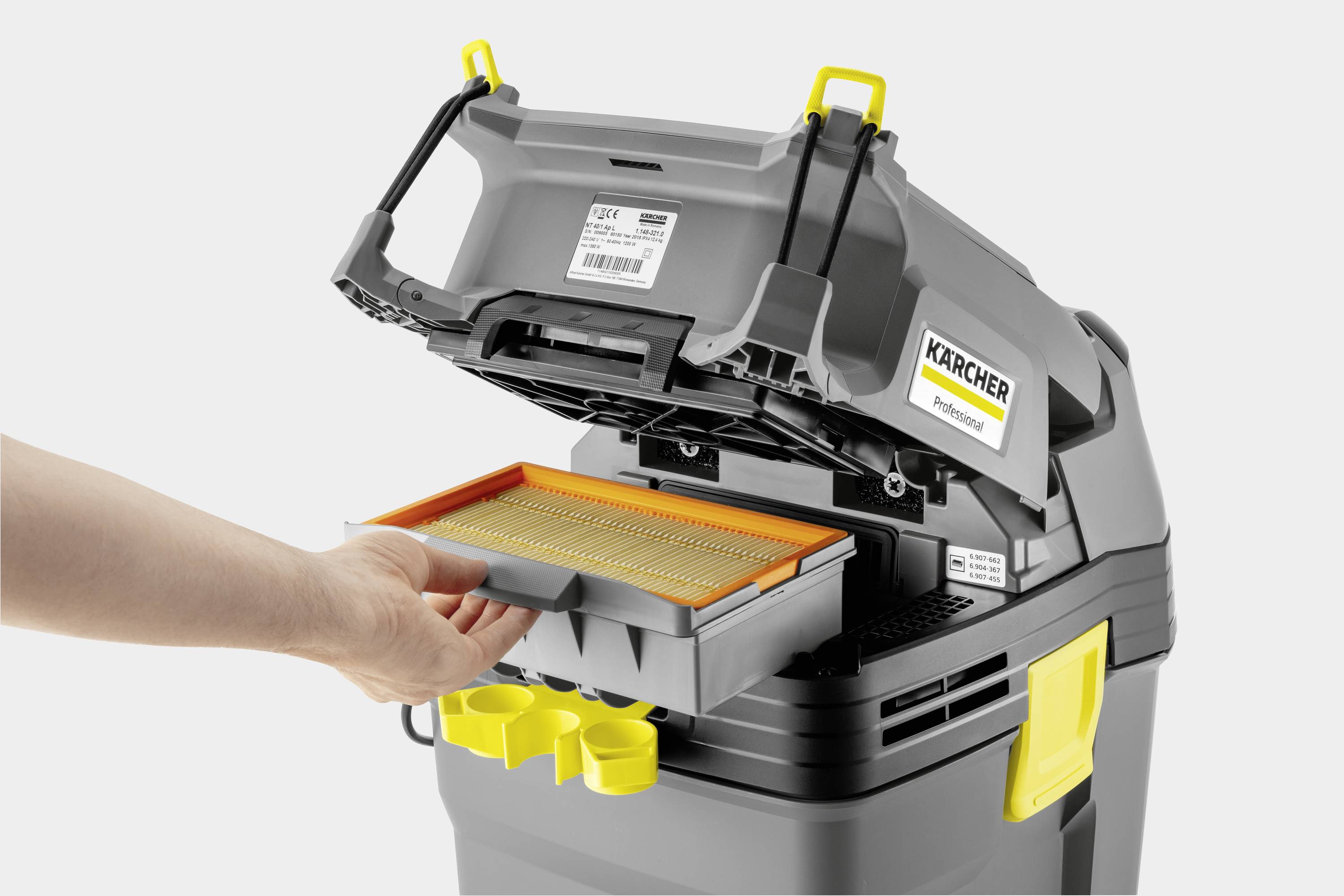 A hand removes the filter from a grey Kärcher vacuum cleaner with an open lid. Yellow details on the device, product label visible.