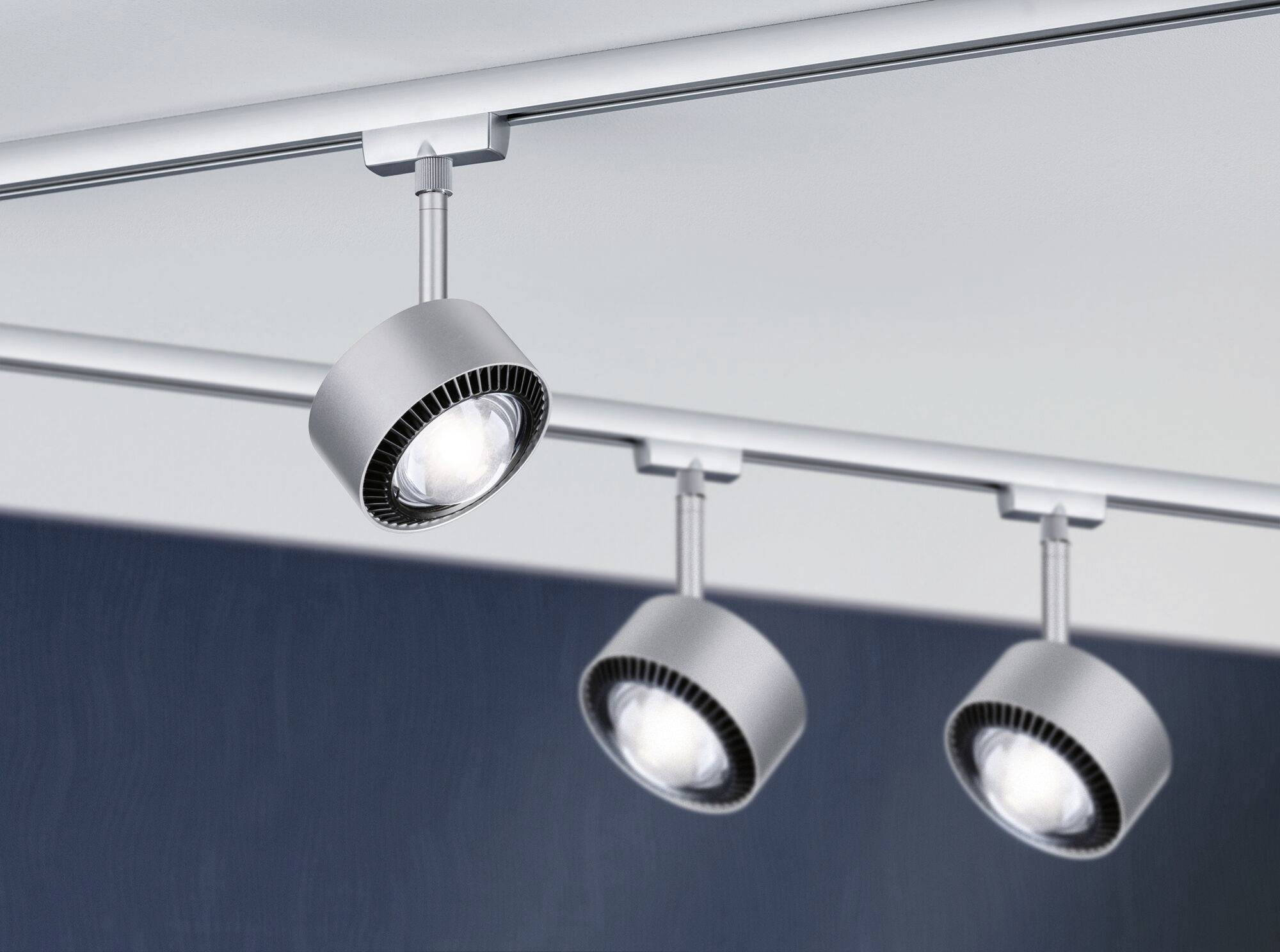 Three silver ceiling spotlights on a track system illuminate a room.