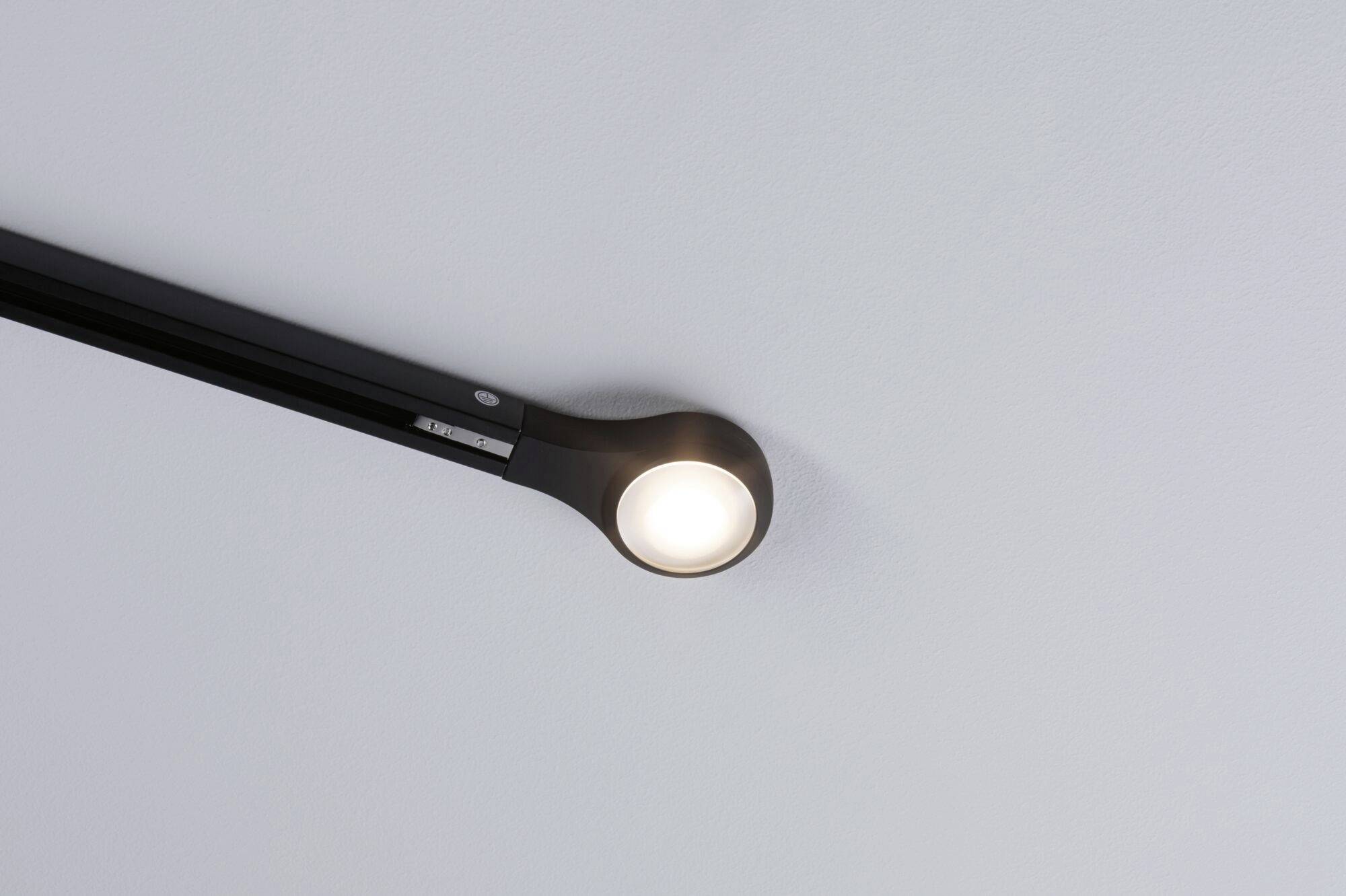 A single ceiling light emits soft light. It is housed in a modern black casing and mounted on a track.