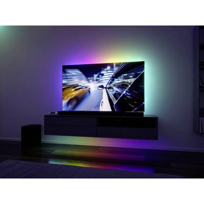 A television on the wall displays a night-time car journey with light effects. The surroundings are bathed in soft, coloured light.