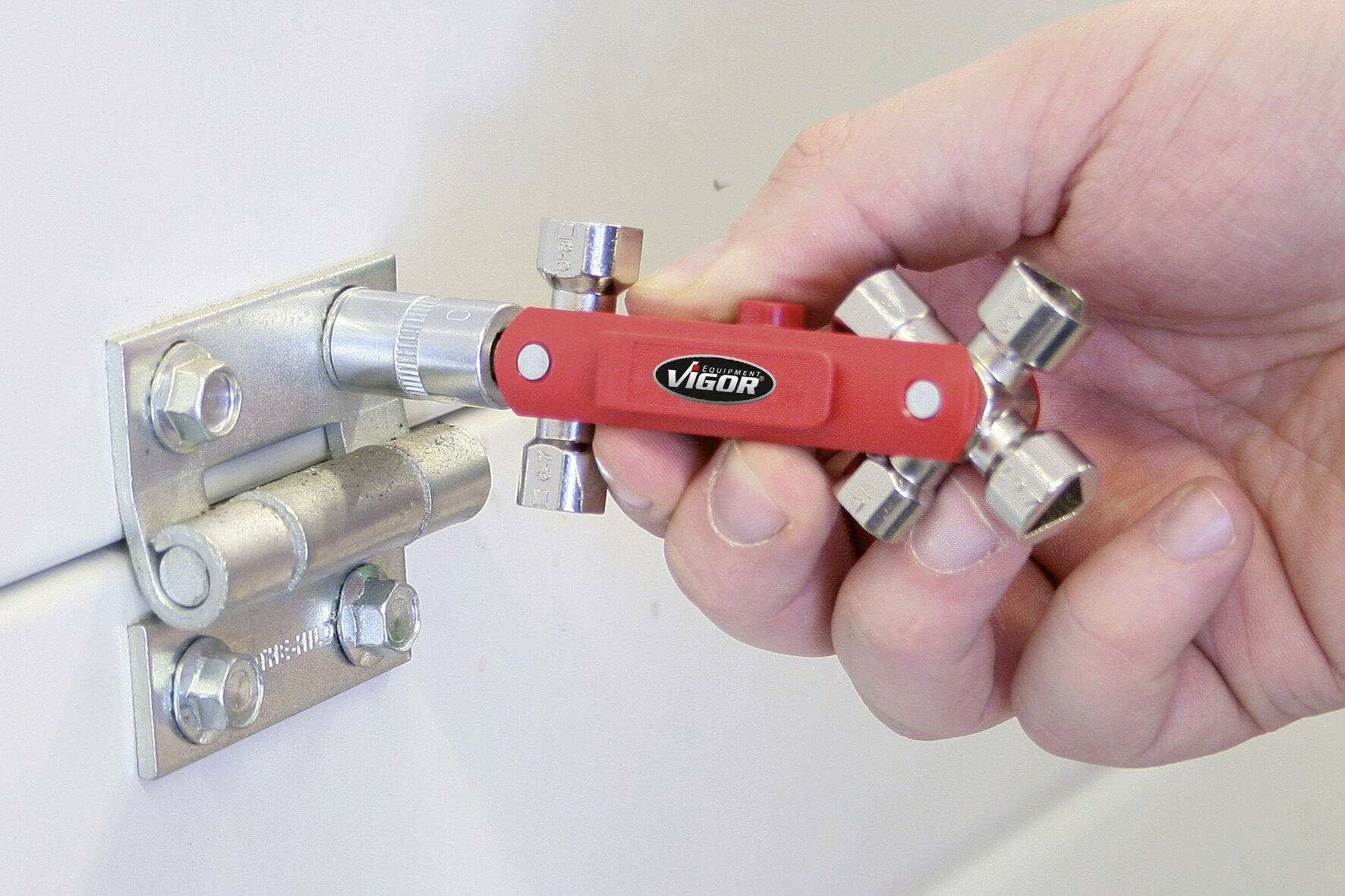 A hand is holding a red torque wrench attached to a metal hinge.