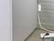 A white cable is plugged into a wall socket, with a grey power strip lying on the floor in front of a grey wall.