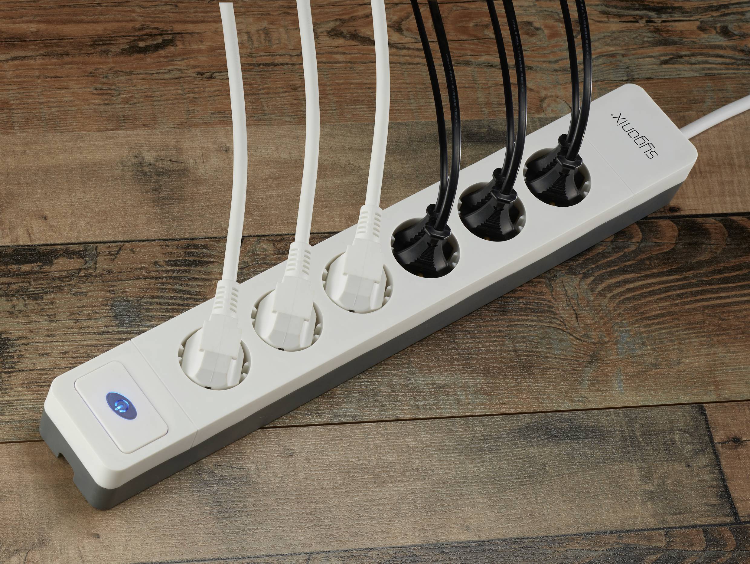 A white six-socket extension lead with three white and two black cables plugged in. Resting on a wooden floor.