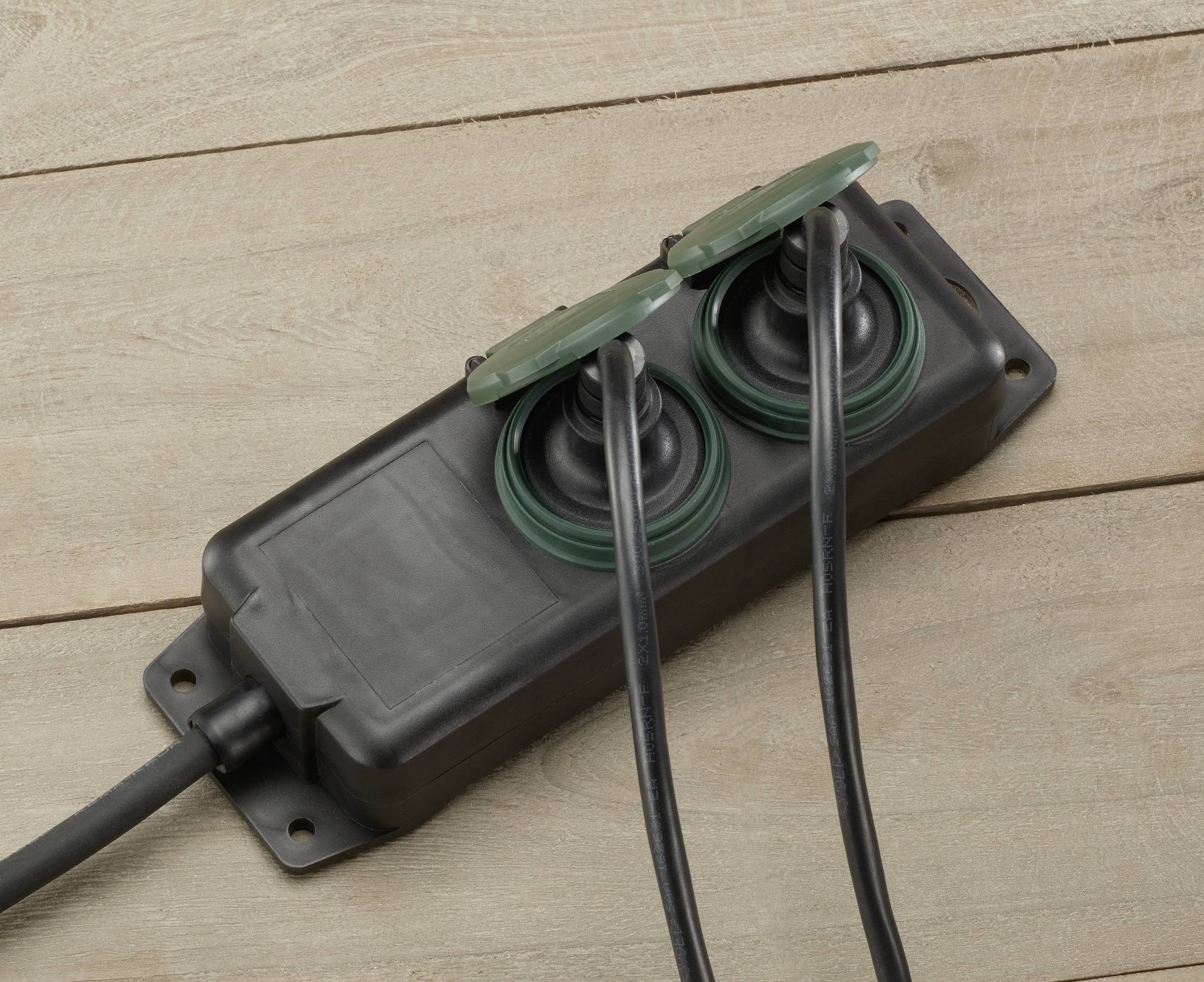 Black, weatherproof extension socket with two covered sockets on a wooden surface. Suitable for outdoor use.