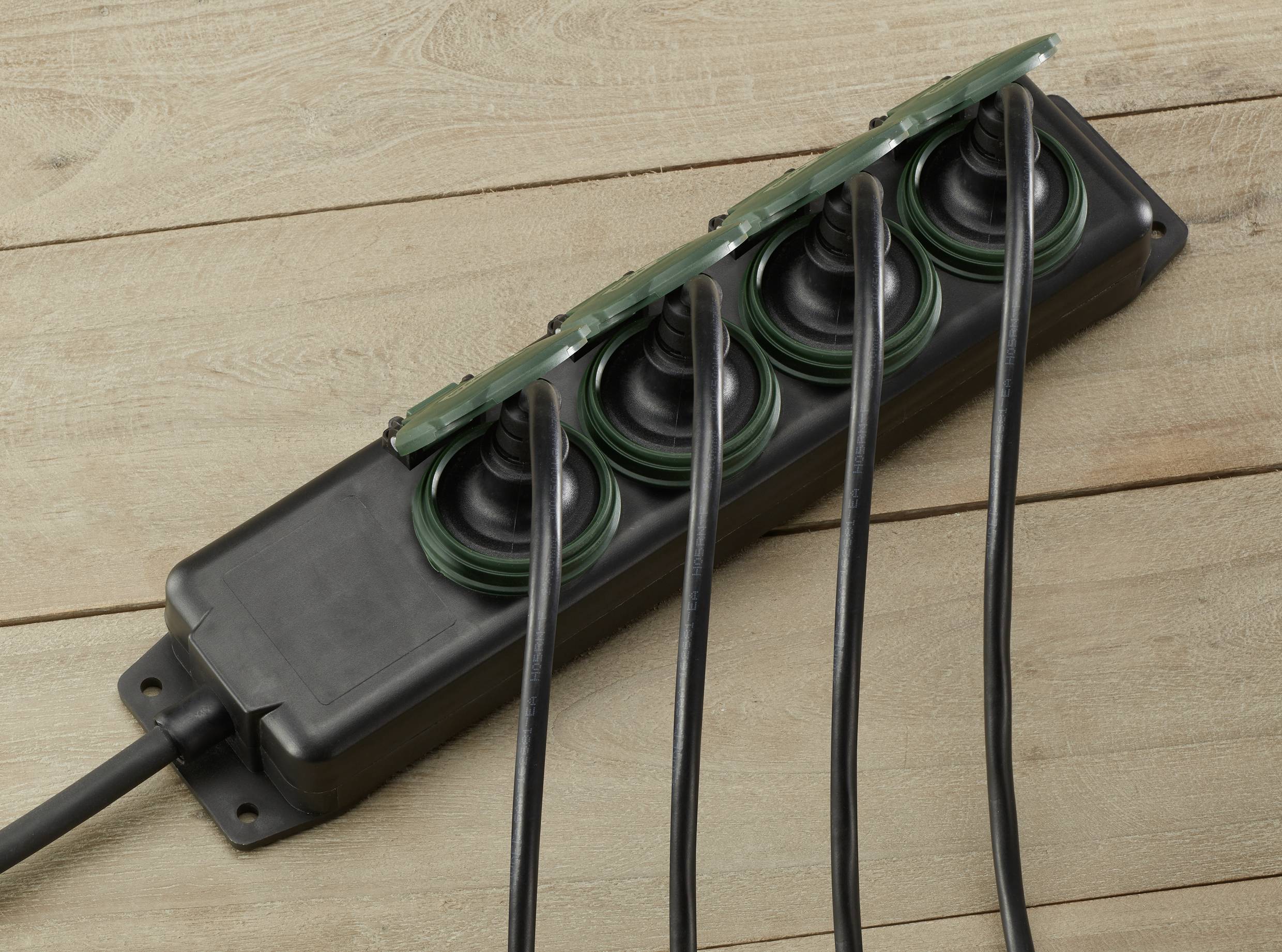 A black multi-socket extension lead with five black cables plugged in is lying on a wooden floor.