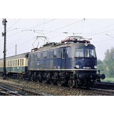 A historic blue electric locomotive is pulling an older train along the tracks. Power lines and trees can be seen in the background.