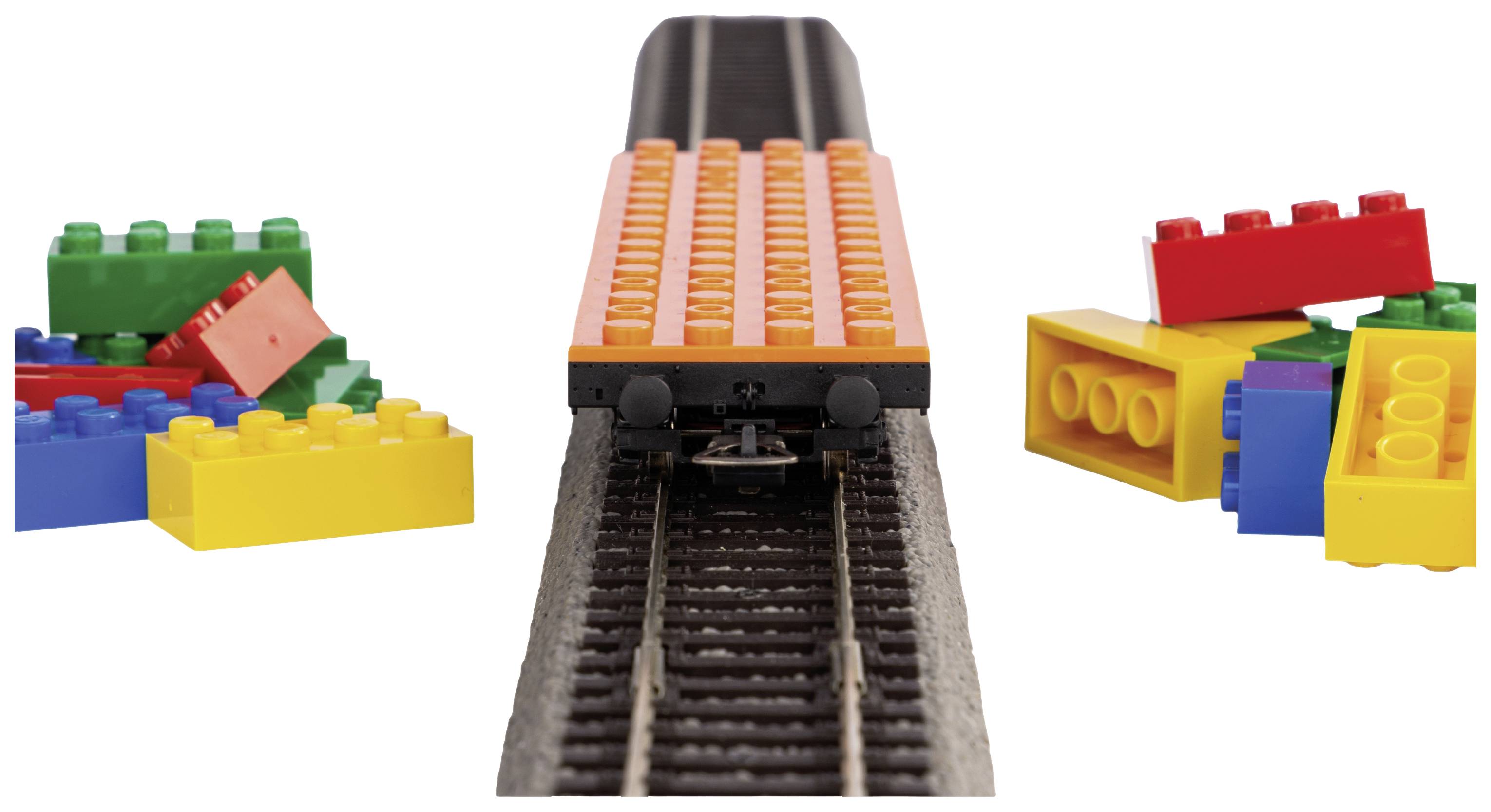 A small train made of building blocks travels on tracks, surrounded by colourful LEGO bricks on both sides.