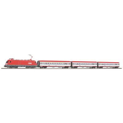 A red model train of the Austrian Federal Railways travels along tracks. It consists of a locomotive and three passenger carriages.