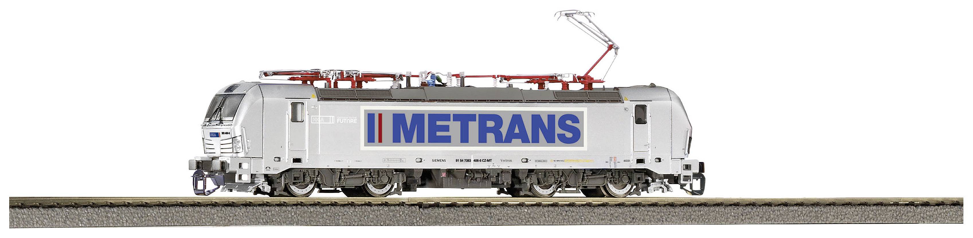 A grey locomotive with the 'METRANS' lettering is travelling on railway tracks. It is modern and equipped with electrical connections.