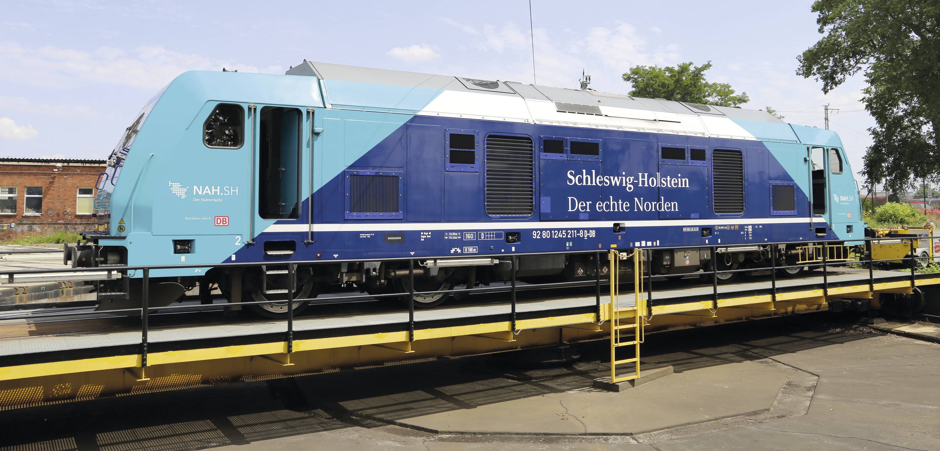 A blue locomotive with the inscription 'Schleswig-Holstein The True North' stands on a turntable outdoors.