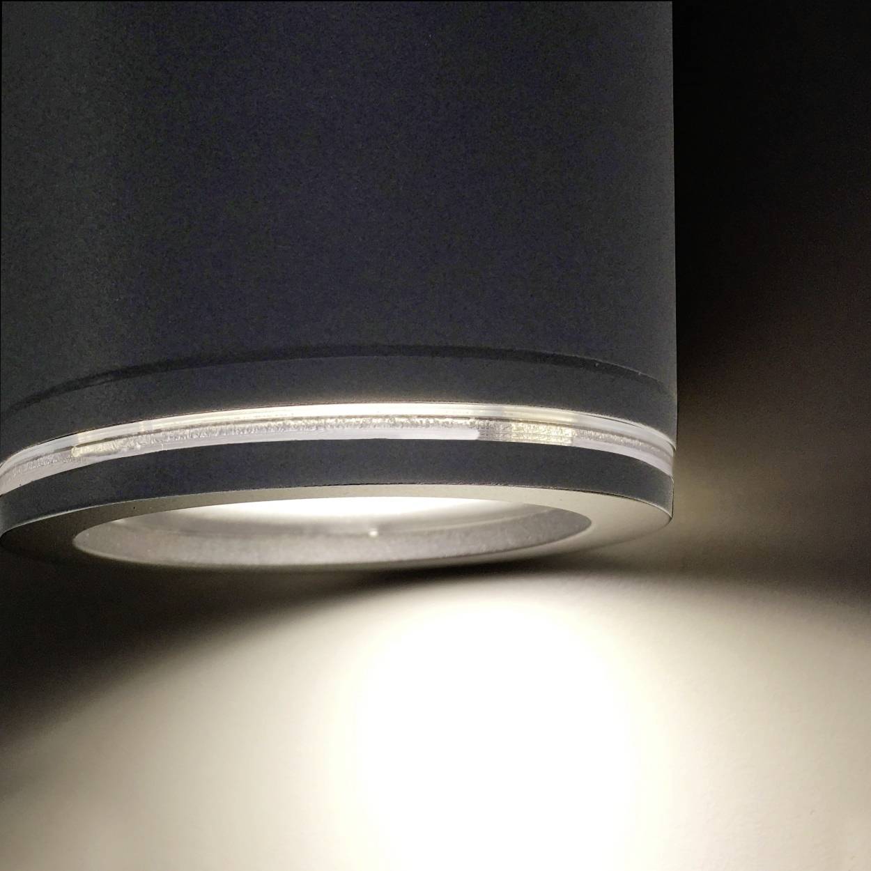 A modern, cylindrical ceiling light shines brightly onto a wall surface.