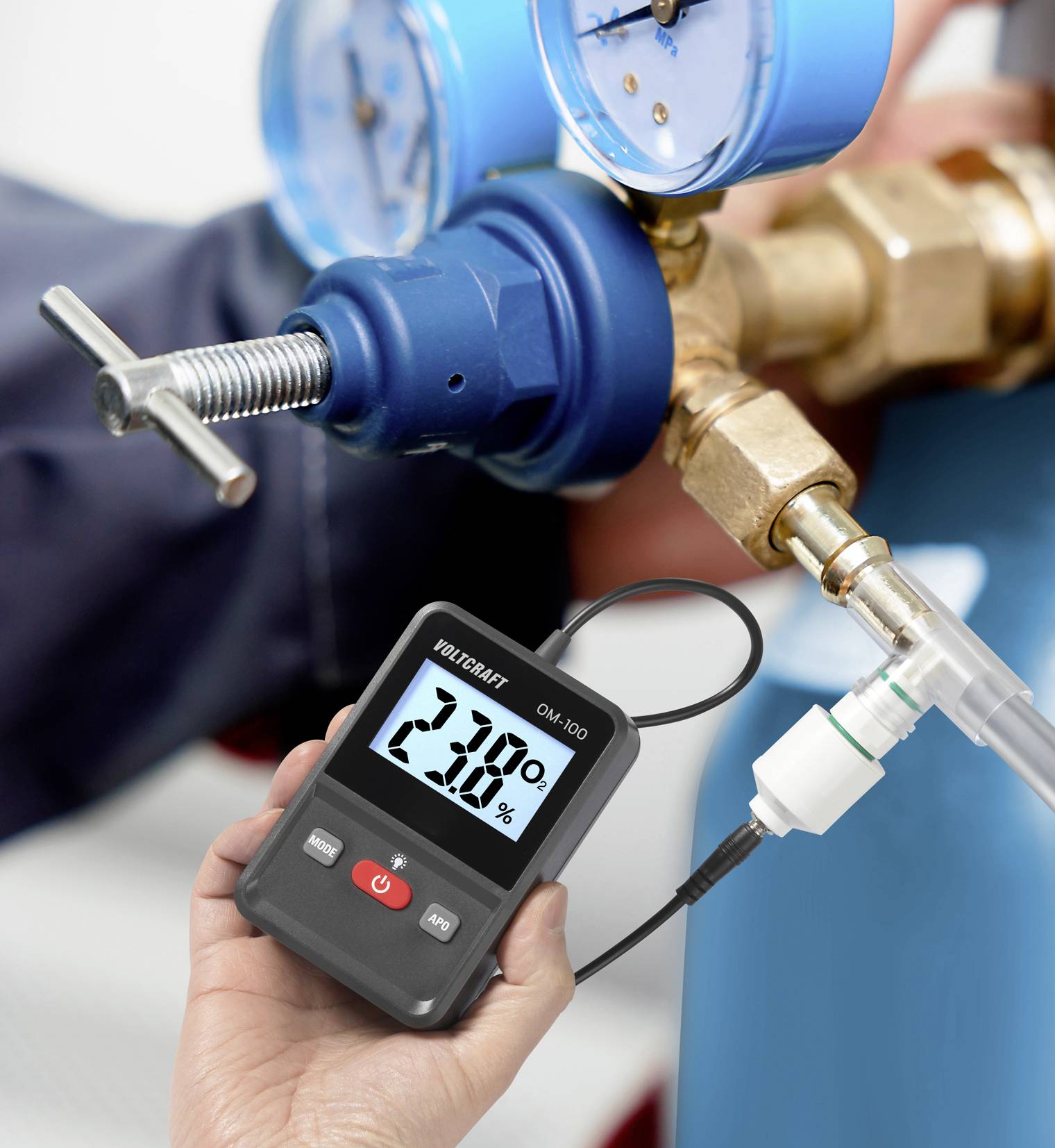 A person is holding a digital measuring device showing a reading of 2.3%. Blue fittings and connections are visible in the background.