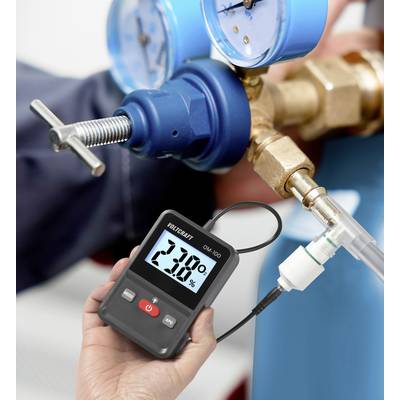 A person is holding a digital measuring device showing a reading of 2.3%. Blue fittings and connections are visible in the background.