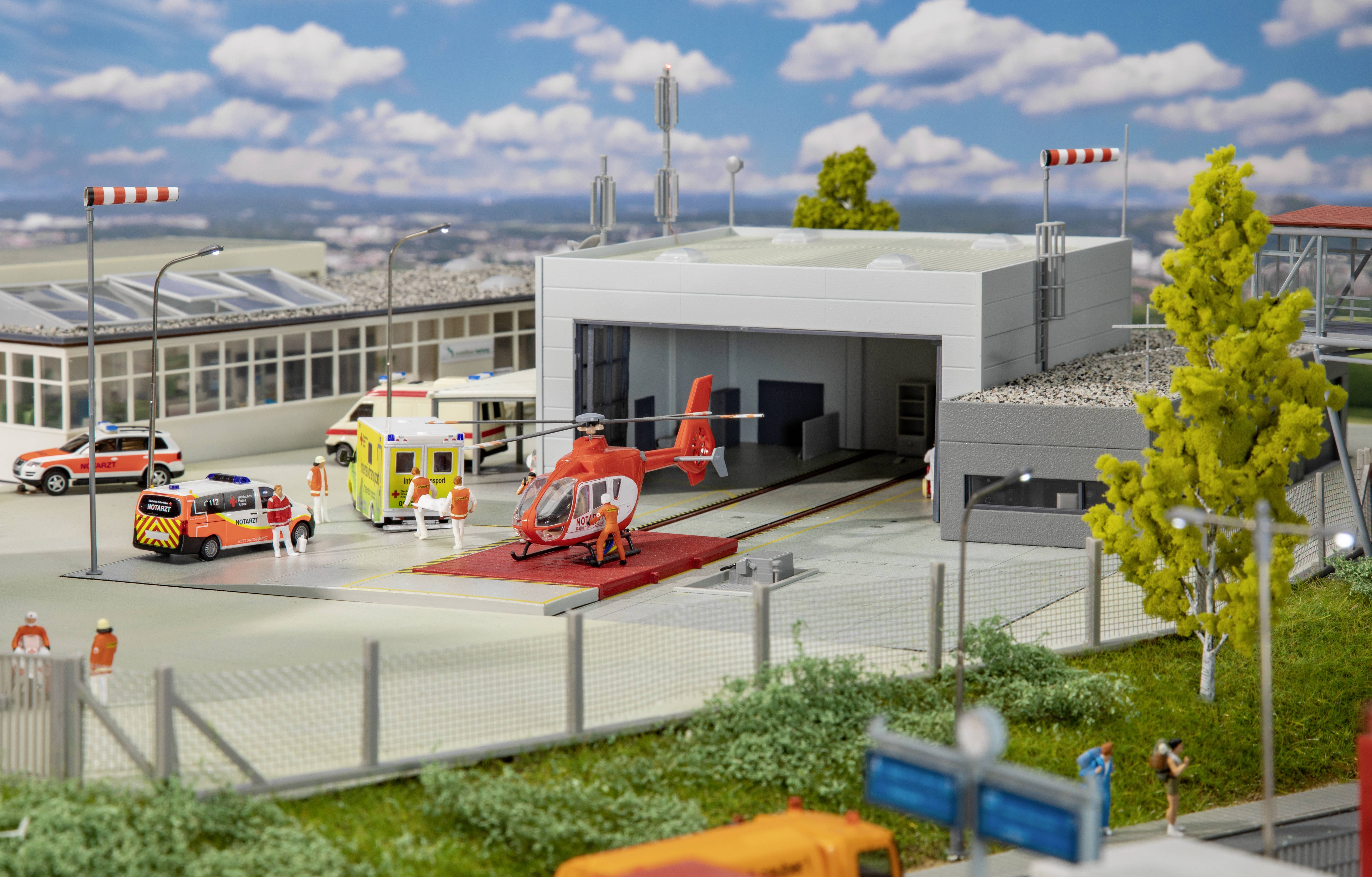 Miniature of a rescue helicopter on a landing platform in front of a building, surrounded by emergency vehicles and figures.